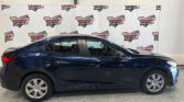 Blue sedan parked indoors in front of a White backdrop with Wheel City Auto Finance Centers logos repeated across it.