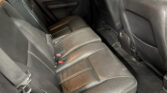 Rear seating area of a car with black leather seats and white contrast stitching, showing seat belts and surrounding panels.