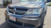 Close-up of a gray Dodge front end at a car dealership, hood reflecting a cloudy sky; Wheel City license plate frame visible in foreground.