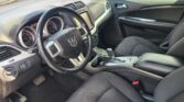 Driver's-seat view of a Dodge SUV interior: steering wheel, instrument cluster, center touchscreen, and gear shifter visible amid black fabric seats.