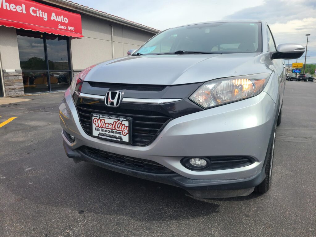 Silver Honda SUV parked at Wheel City Auto dealership under a red awning.