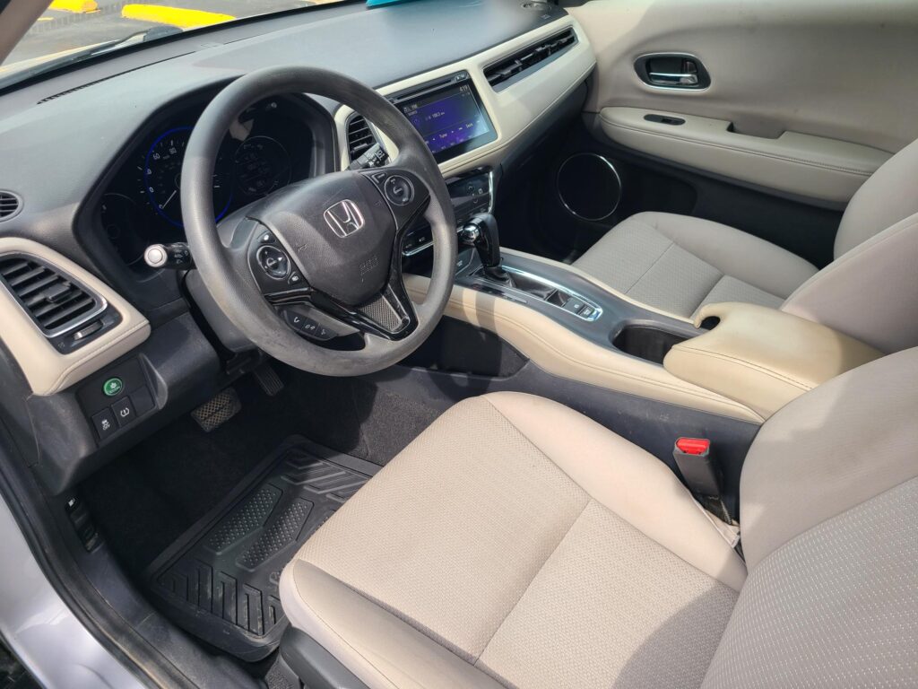 Interior of a car showing the steering wheel, touchscreen display, and beige seats from the driver’s side passenger area