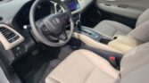 Interior of a car showing the steering wheel, touchscreen display, and beige seats from the driver’s side passenger area