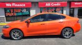Orange sedan parked in front of a storefront with red signage reading 'We Finance' and 'All Credit' under a clear blue sky.