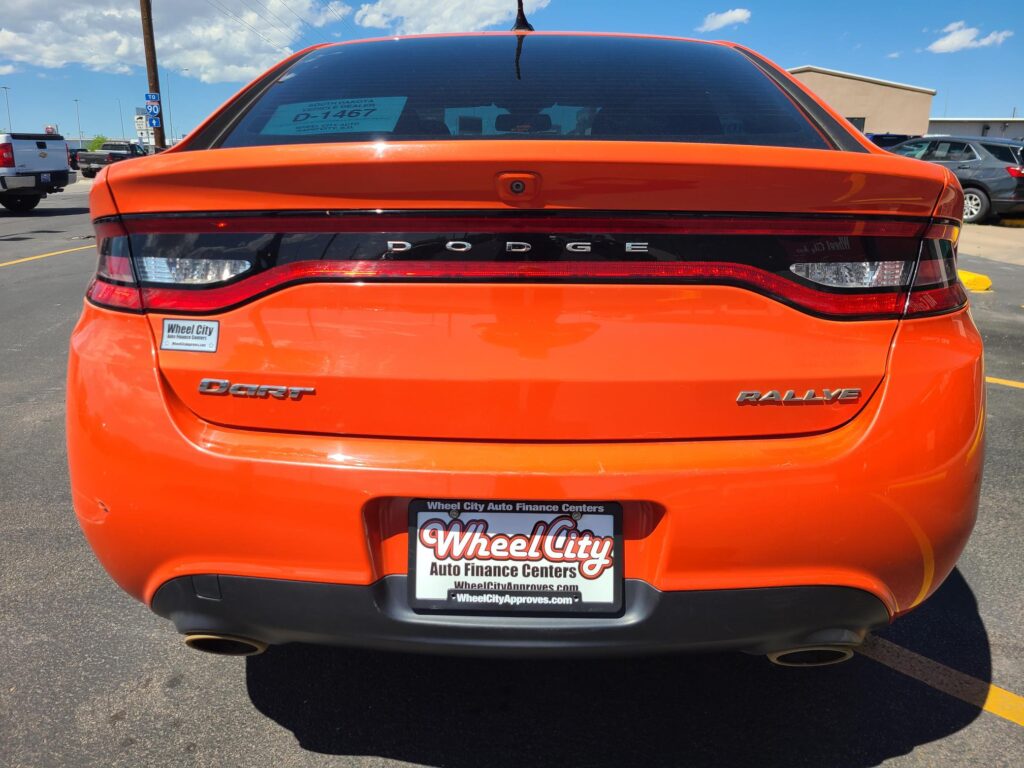 Rear view of an orange Dodge Dart Rallye in a parking lot, with dealer plate and Wheel City sticker visible on the bumper.