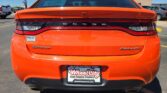 Rear view of an orange Dodge Dart Rallye in a parking lot, with dealer plate and Wheel City sticker visible on the bumper.