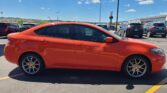 Bright orange sedan parked in a busy parking lot on a sunny day, with other cars and a building in the background.