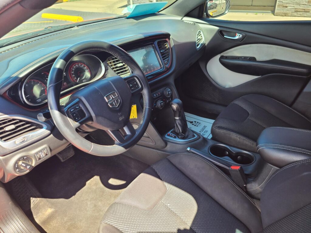 Interior of a car showing the steering wheel, dashboard, center touchscreen, gear shifter, and front seats in black fabric.