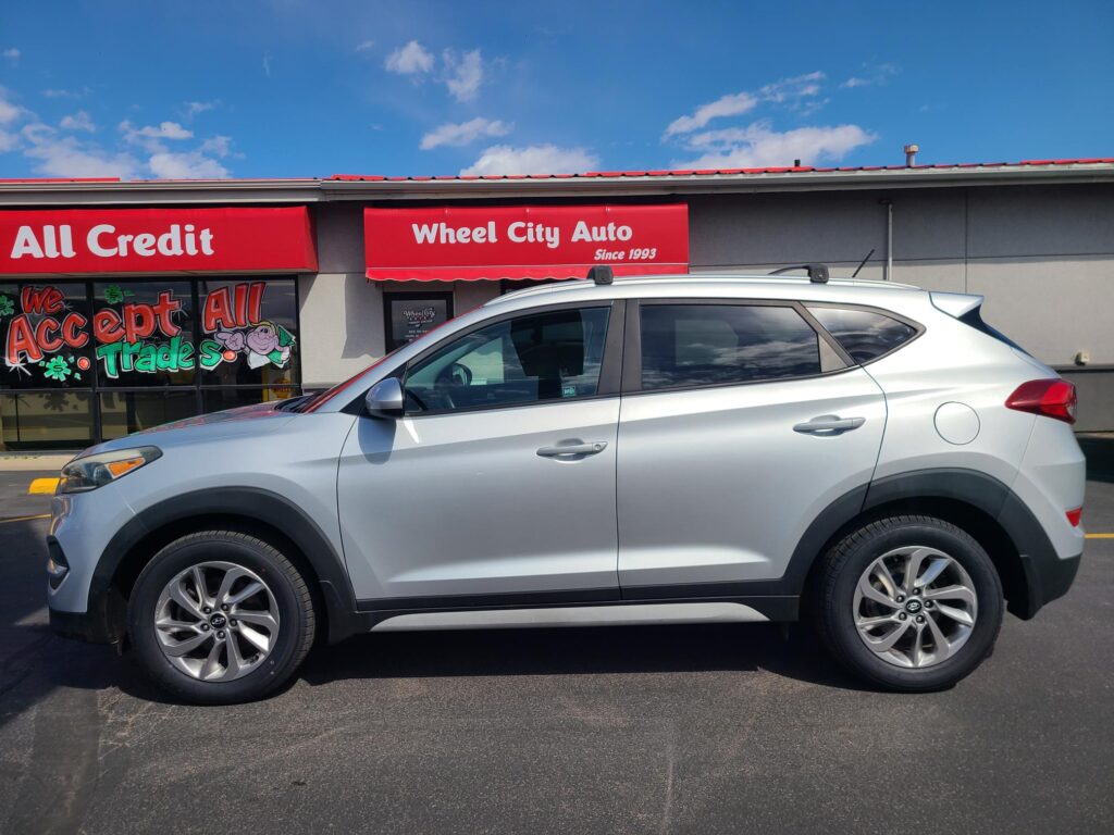 Silver SUV parked in front of Wheel City Auto dealership with red 'All Credit' and 'Since 1993' signs.