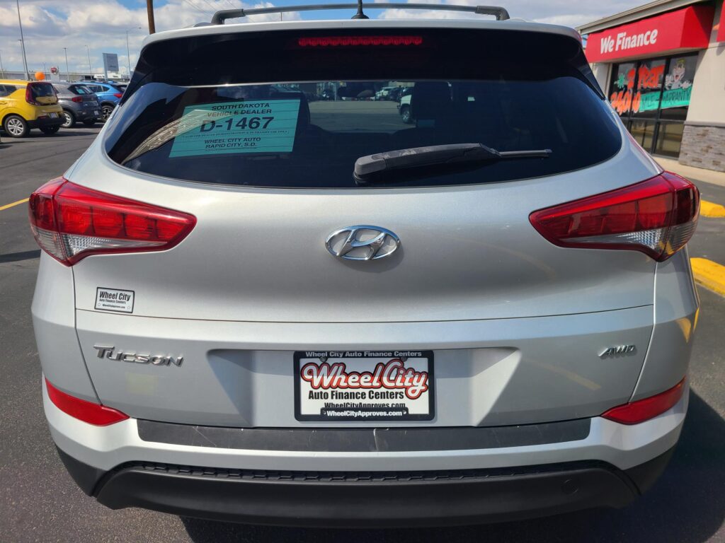 Rear view of a silver Hyundai Tucson in a car dealership lot with Wheel City license plate frame and Window sticker visible on the rear window.