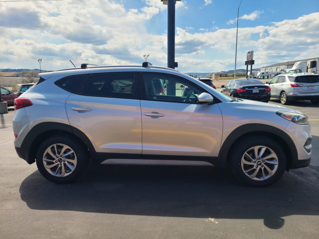 Side view of a white SUV in a parking lot, with other cars and a blue sky with clouds.