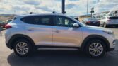 Side view of a white SUV in a parking lot, with other cars and a blue sky with clouds.