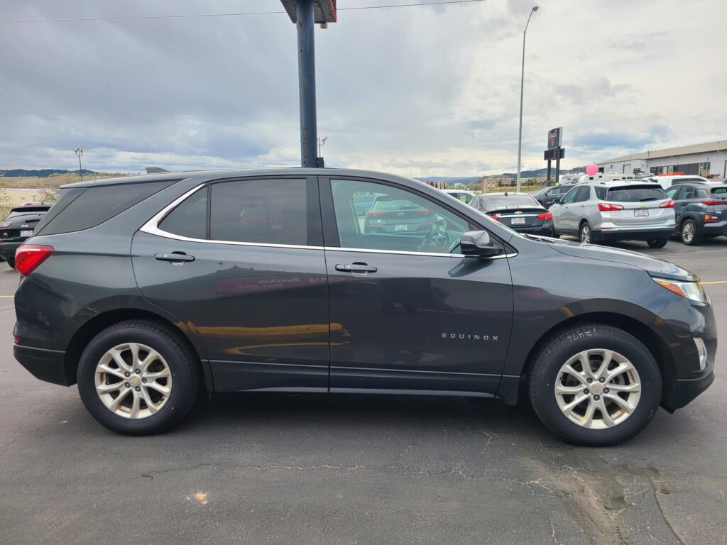 Side view of a dark gray Chevrolet Equinox parked in a car lot with other vehicles nearby under a cloudy sky? (informative image)