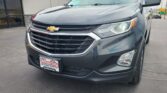 Close-up of a gray Chevrolet SUV parked outside a dealership, showing the front grille, headlight, and Chevy emblem with a Wheel City Auto Finance Centers license plate frame visible.