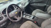 View of the car's black interior: steering wheel, center touchscreen, gear selector, and front passenger seat in front of you