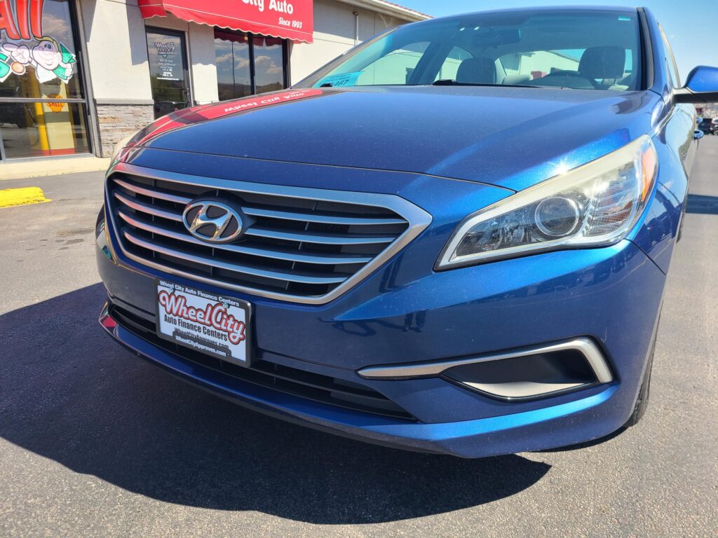 Close-up of a blue Hyundai SUV parked in front of a car dealership, showing the grille and headlight.