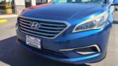 Close-up of a blue Hyundai SUV parked in front of a car dealership, showing the grille and headlight.