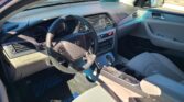 Front interior of a car showing the steering wheel, dashboard, center console, and light gray seats in daylight.