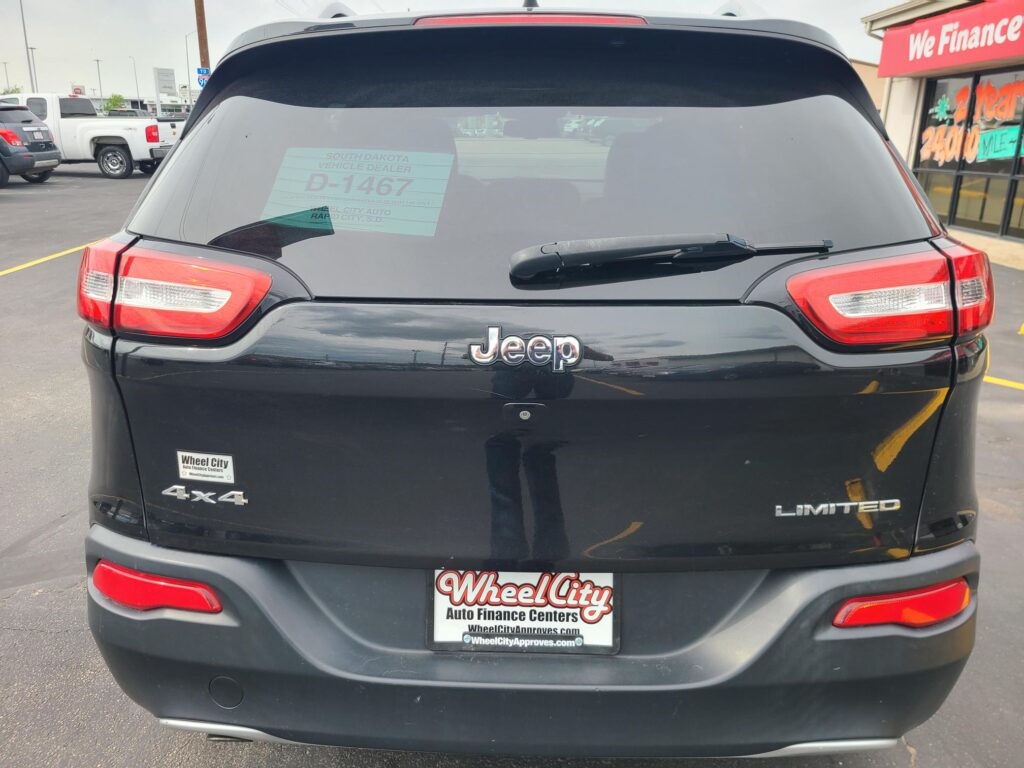 Rear view of a black Jeep SUV with 'LIMITED' and '4x4' badges, dealer plate reading Wheel City Auto Finance Centers, in a car lot.