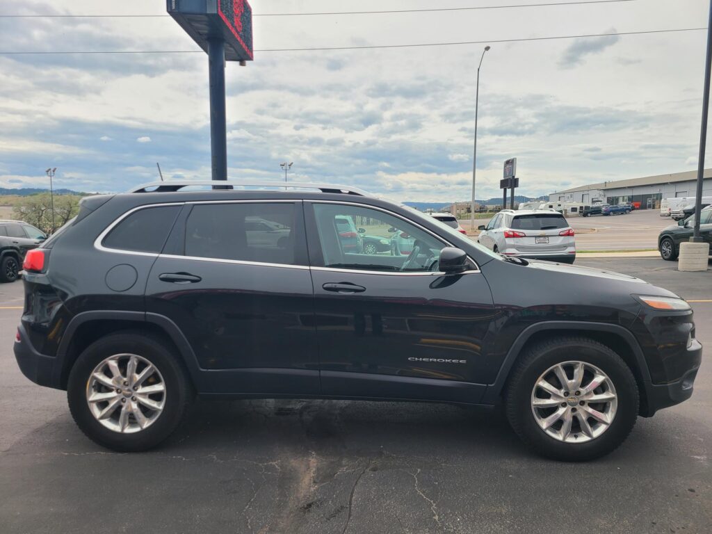 Side view of a dark blue Jeep Cherokee SUV in a parking lot, with other cars and a building in the background.