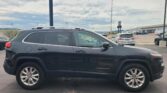 Side view of a dark blue Jeep Cherokee SUV in a parking lot, with other cars and a building in the background.