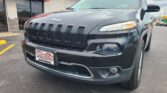 Close-up view of a dark gray Jeep SUV parked in front of a Wheel City Auto dealership, featuring the seven-slot grille and modern headlights.