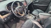 Front interior of a black leather Jeep, featuring the steering wheel, center touchscreen, gear shifter, and leather seats.