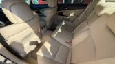 Light beige car interior with a spacious rear seating area, showing three seats, a center armrest, and seat belts visible.