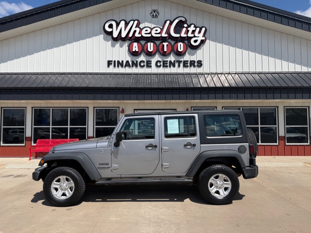 Silver Jeep Wrangler parked in front of Wheel City Auto Finance Centers storefront on a sunny day.