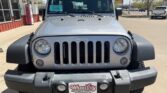 Front view of a silver Jeep Wrangler with round headlights and seven-slot grille in a dealership lot.