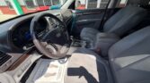 Front interior of a car showing steering wheel, center console, and two front seats bathed in sunlight, with a dealership backdrop outside the windows.