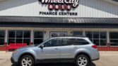 Side view of a silver SUV parked in front of Wheel City Auto Finance Centers, with a red bench and large storefront windows visible.