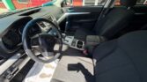 Front interior of a car from the driver's seat, showing steering wheel, dashboard, and center console with black fabric seats outside scenery through windows.