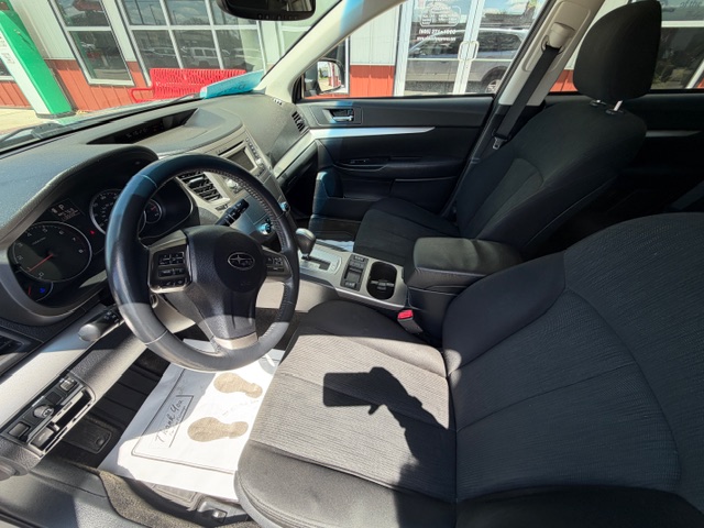 Front interior of a car from the driver's seat, showing steering wheel, dashboard, and center console with black fabric seats outside scenery through windows.
