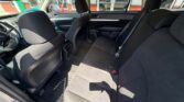 Interior of a black cloth-seat car viewed from the rear passenger side, showing front seats, center console, and a back bench with seat belts; sunlight through windows.