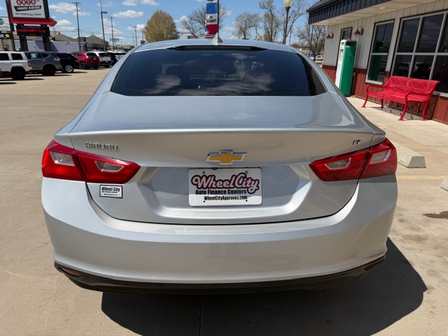 Rear view of a silver Chevrolet sedan parked at a dealership, showing the Chevrolet badge and a Wheel City Auto Finance Centers license plate frame on the trunk.