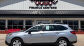 Silver Subaru Outback SUV parked in front of Wheel City Auto Finance Centers storefront on a sunny day, dealership signage visible in background.