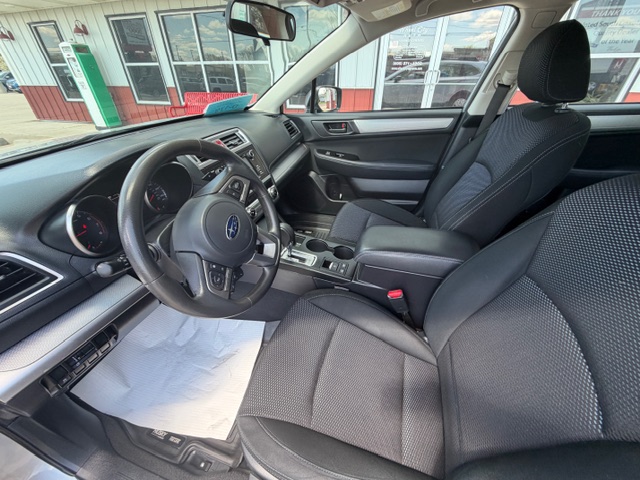 Interior of a Subaru sedan: steering wheel with logo, dashboard, gear shift, and front seats from the driver’s side perspective