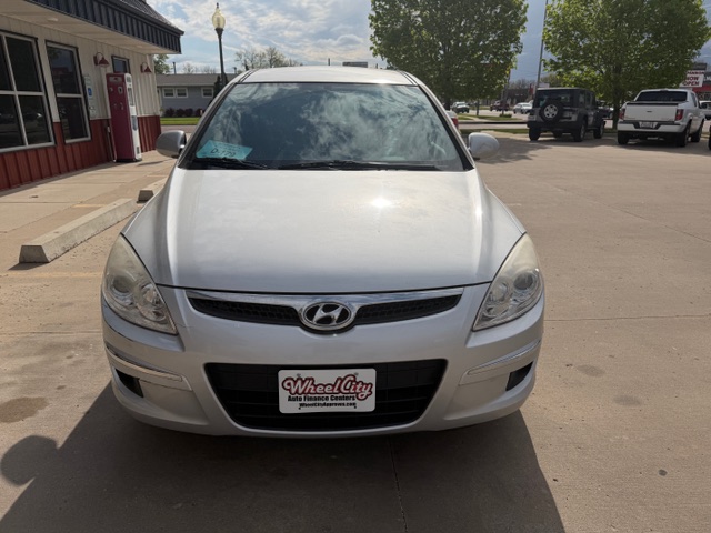 Front view of a silver Hyundai SUV parked in a parking lot near a storefront. A dealership license plate is visible on the bumper.
