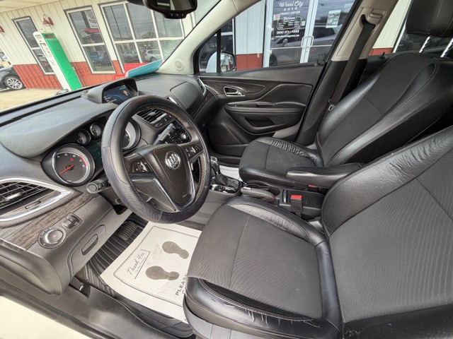 Black leather front seats and steering wheel of a car interior with a center console and dashboard, showing a gear shifter and floor mats.