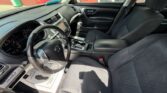 Interior of a dark gray Nissan sedan’s front cabin: steering wheel, dashboard, center console, and front seats visible in daylight.