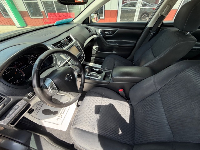 Interior of a dark gray Nissan sedan’s front cabin: steering wheel, dashboard, center console, and front seats visible in daylight.