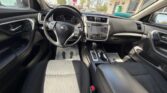 Front interior of a Nissan car: steering wheel, dashboard, center touchscreen, gear shifter, and front seats from the passenger side perspective.
