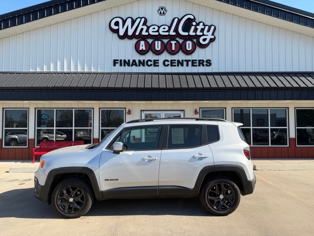 Silver Jeep Renegade SUV parked in front of Wheel City Auto Finance Centers storefront in a dealership lot.