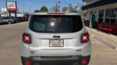 Rear view of a silver Jeep SUV parked in a dealership lot, showing a Wheel City license plate frame and red taillights.