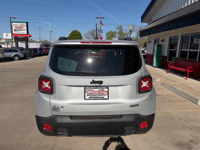 Rear view of a silver Jeep SUV parked in a dealership lot, showing a Wheel City license plate frame and red taillights.