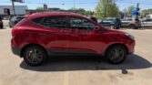 Red crossover SUV parked in a dealership lot, left-side profile with other cars and buildings in the background.