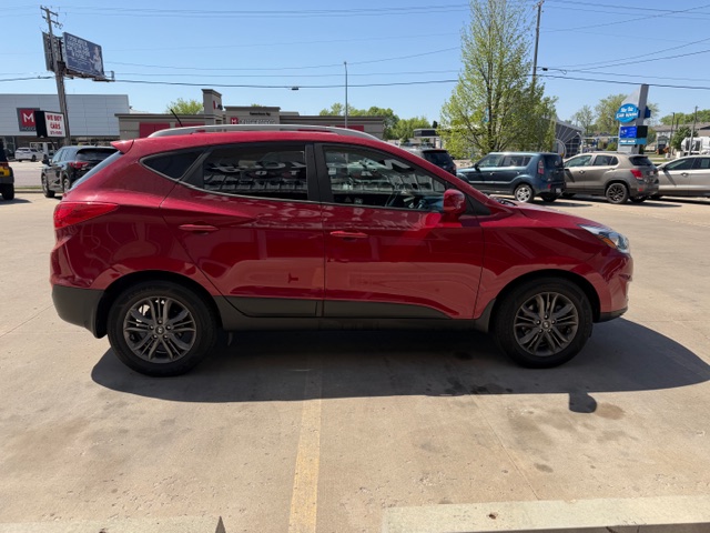 Red crossover SUV parked in a dealership lot, left-side profile with other cars and buildings in the background.