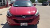 Front view of a red Hyundai SUV parked in a lot near a storefront on a sunny day.