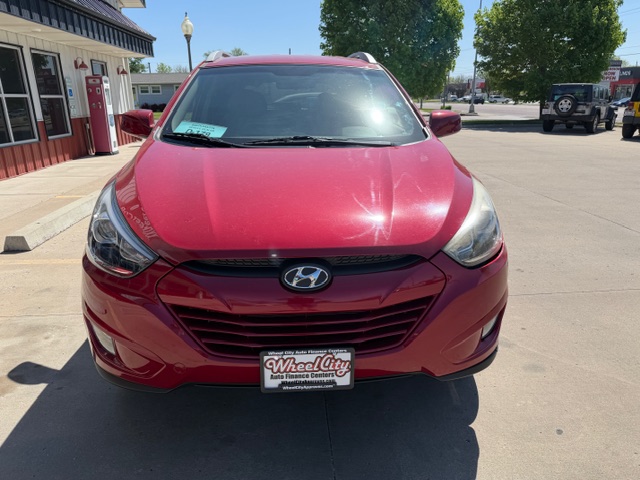 Front view of a red Hyundai SUV parked in a lot near a storefront on a sunny day.